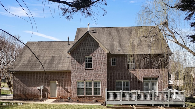 rear view of property featuring brick siding, a shingled roof, and a deck