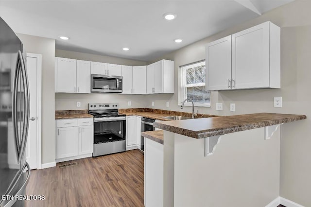 kitchen with a kitchen bar, a sink, wood finished floors, appliances with stainless steel finishes, and a peninsula