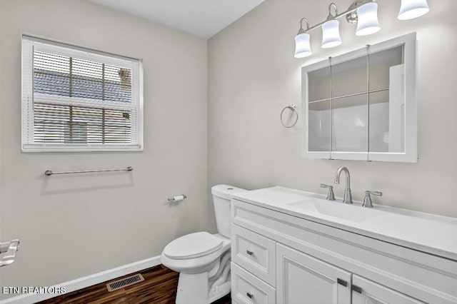 bathroom featuring visible vents, baseboards, toilet, wood finished floors, and vanity