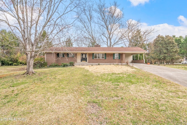 ranch-style home with brick siding, a front yard, a chimney, a carport, and driveway