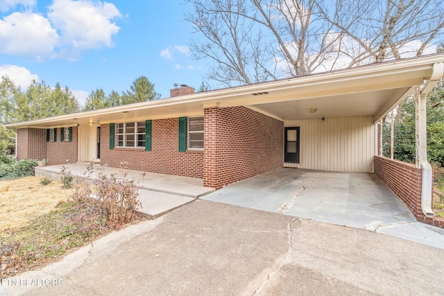 single story home featuring an attached carport, brick siding, driveway, and a chimney