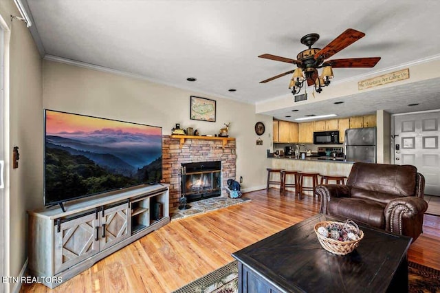 living room with wood finished floors, baseboards, a fireplace, ceiling fan, and ornamental molding