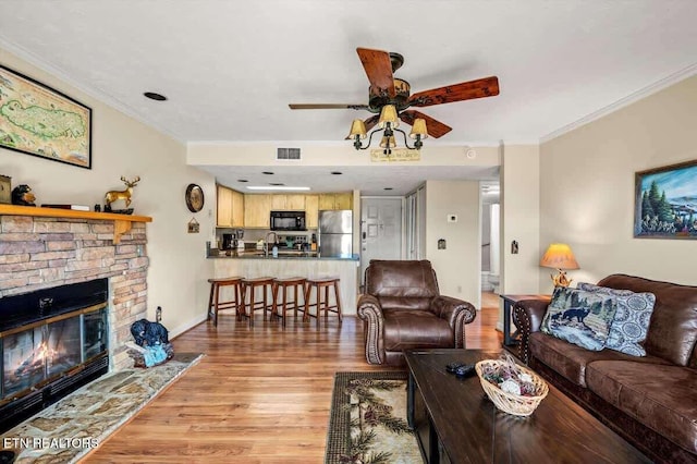 living area with visible vents, light wood-style flooring, a stone fireplace, and crown molding