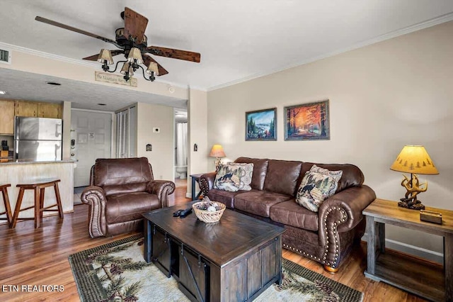 living room with ceiling fan, visible vents, light wood-style flooring, and crown molding