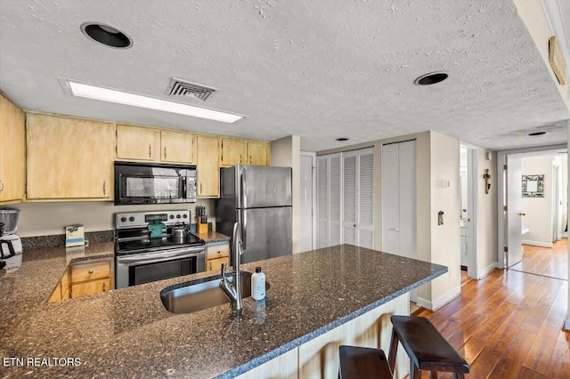 kitchen featuring visible vents, light brown cabinetry, a sink, hardwood / wood-style floors, and appliances with stainless steel finishes