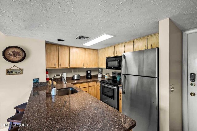 kitchen with dark stone counters, a peninsula, stainless steel appliances, a textured ceiling, and a sink