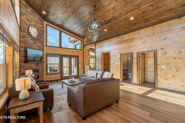 living area featuring wooden walls, wood ceiling, a stone fireplace, a towering ceiling, and wood finished floors