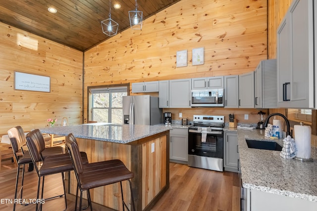 kitchen featuring a kitchen bar, a sink, a kitchen island, stainless steel appliances, and wooden walls