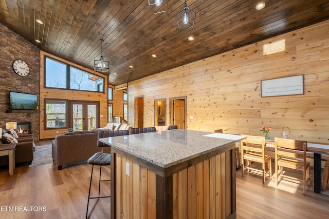 kitchen with wooden walls, a kitchen island, wooden ceiling, light wood-style floors, and high vaulted ceiling