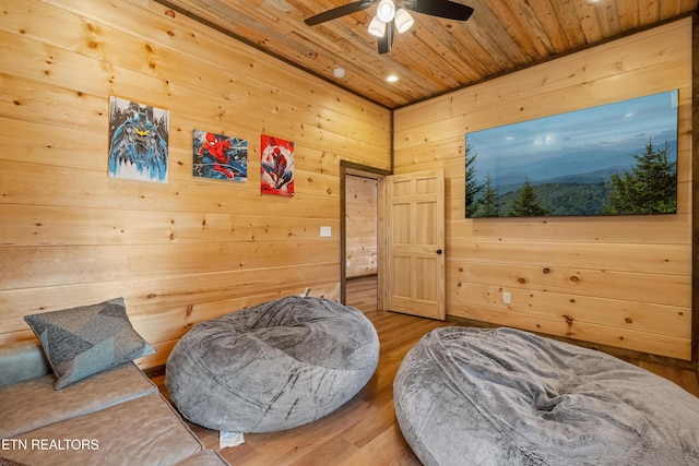 sitting room with wooden walls, wood ceiling, a ceiling fan, and wood finished floors