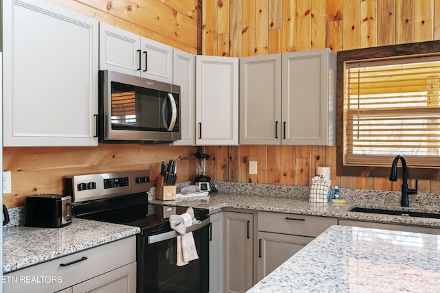 kitchen featuring wood walls, light stone counters, white cabinets, stainless steel appliances, and a sink