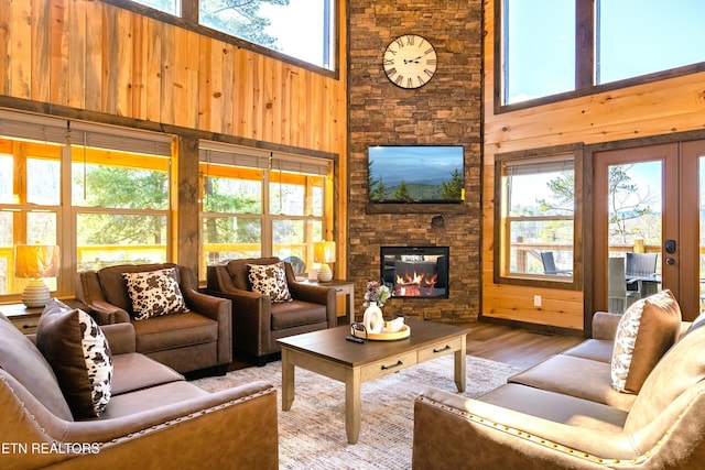 living area featuring a stone fireplace, wood walls, a towering ceiling, and wood finished floors