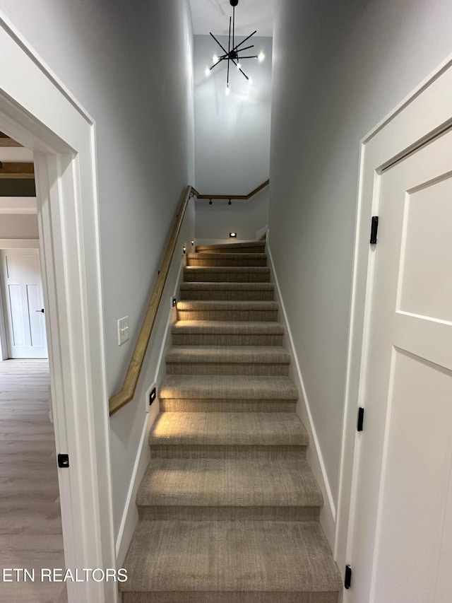 stairway with wood finished floors, baseboards, and a chandelier