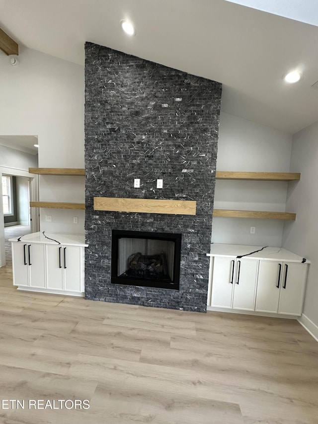 unfurnished living room featuring a stone fireplace, lofted ceiling, and light wood-style floors