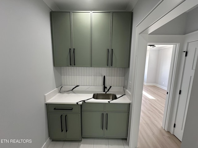 kitchen with a sink, light countertops, light wood-style floors, green cabinets, and backsplash