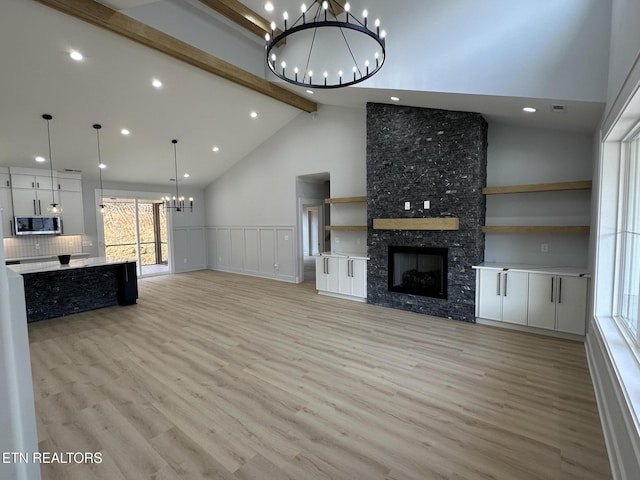 living area featuring beam ceiling, light wood-style flooring, a fireplace, and an inviting chandelier