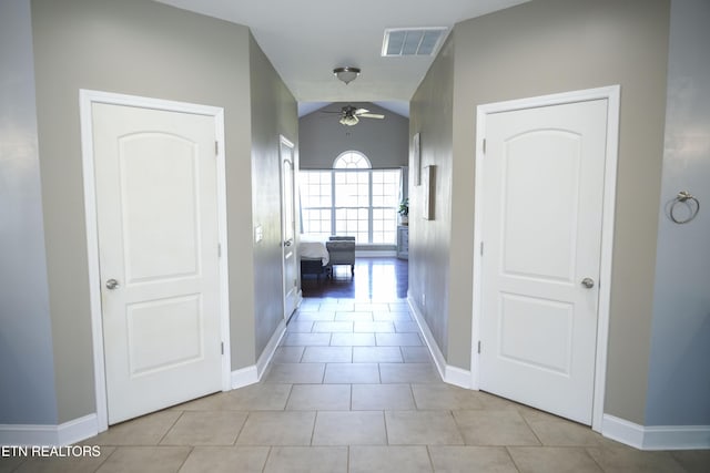 hallway with tile patterned floors, baseboards, visible vents, and lofted ceiling