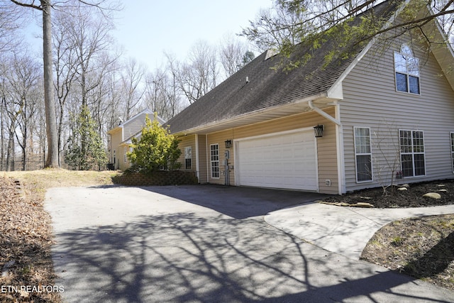 view of side of home with aphalt driveway, an attached garage, and a shingled roof