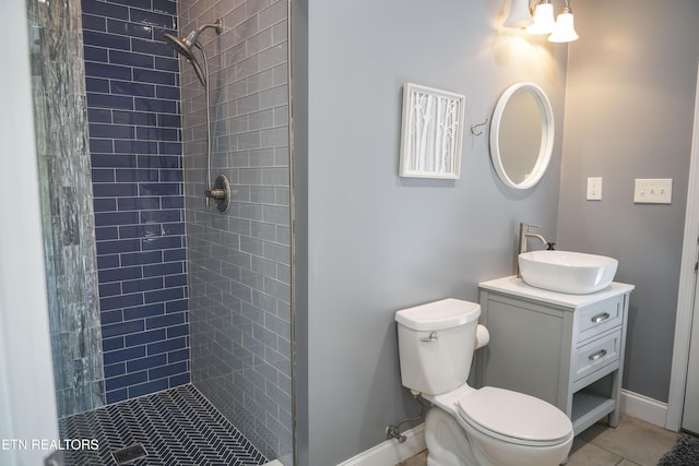 bathroom with toilet, tiled shower, vanity, and baseboards