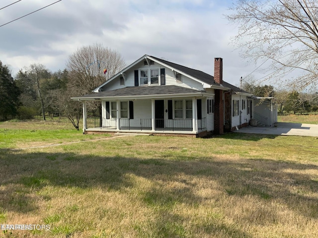 country-style home with covered porch, a chimney, a front yard, and a shingled roof