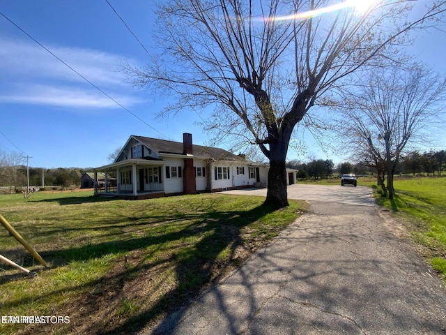 view of front of property with aphalt driveway, a chimney, a porch, and a front lawn