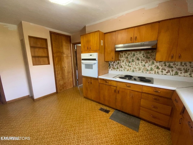 kitchen featuring oven, electric cooktop, under cabinet range hood, brown cabinetry, and light countertops