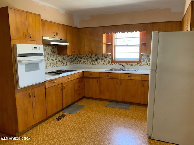 kitchen with visible vents, under cabinet range hood, a sink, white appliances, and light floors