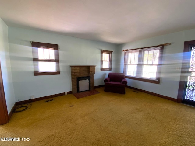 unfurnished living room with a wealth of natural light, visible vents, a brick fireplace, and carpet flooring