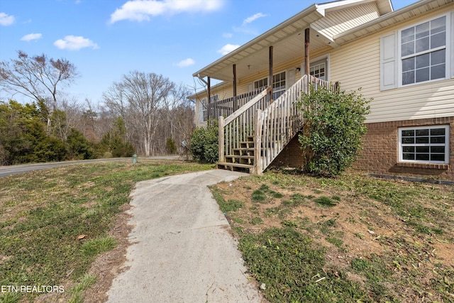 view of side of home featuring brick siding, stairway, and covered porch