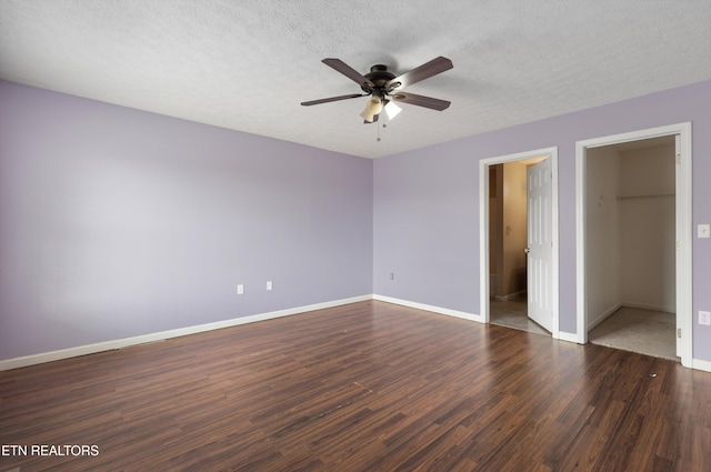 unfurnished bedroom with baseboards, a textured ceiling, dark wood-style floors, and a spacious closet