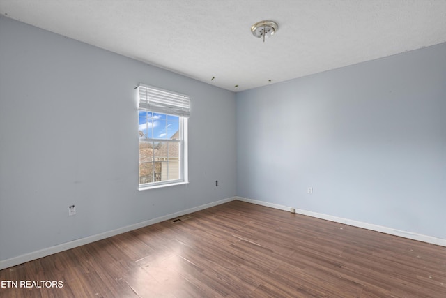 spare room with visible vents, baseboards, a textured ceiling, and dark wood-style floors