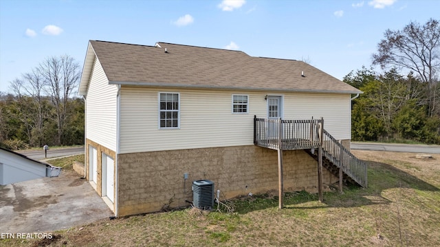 back of house featuring stairway, central AC unit, a garage, and roof with shingles