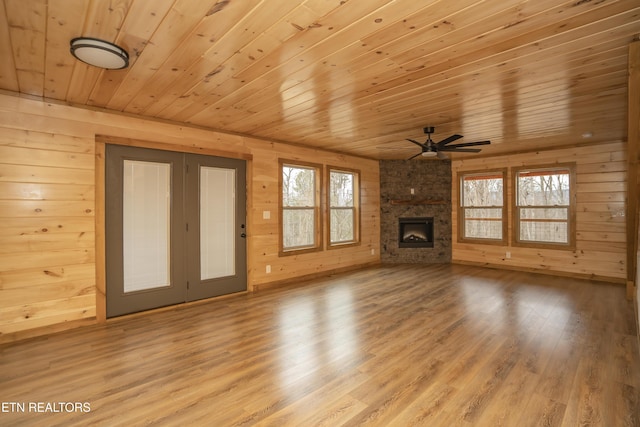 unfurnished living room featuring wood finished floors, a large fireplace, wooden ceiling, wood walls, and ceiling fan