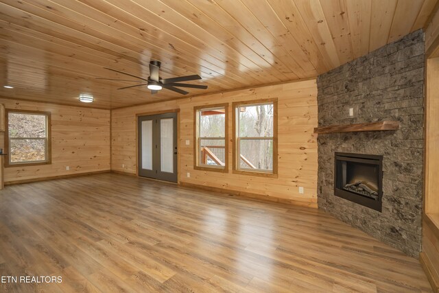 unfurnished living room featuring a stone fireplace, wooden ceiling, wood finished floors, and a healthy amount of sunlight