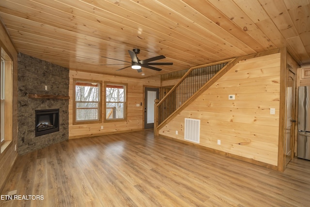 unfurnished living room with visible vents, wood ceiling, stairs, a stone fireplace, and wood finished floors