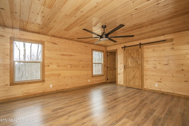 unfurnished room with wood finished floors, a barn door, wooden walls, wooden ceiling, and ceiling fan