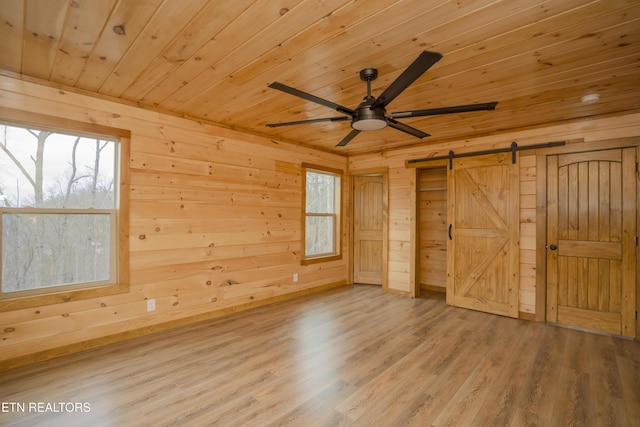 unfurnished bedroom with a barn door, wooden walls, wood ceiling, and wood finished floors