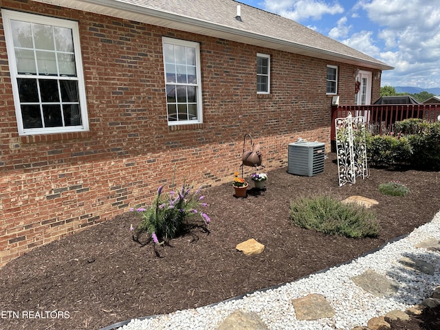 view of side of property with brick siding, cooling unit, and a shingled roof