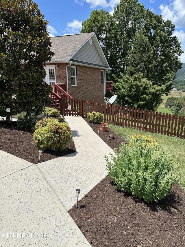 view of property exterior with fence, brick siding, and roof with shingles