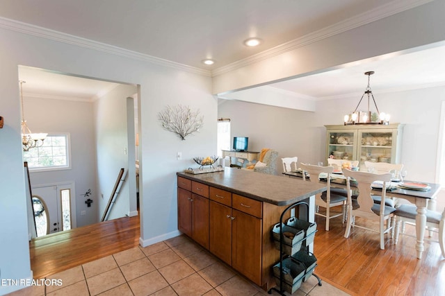 kitchen with dark countertops, crown molding, brown cabinets, a peninsula, and a notable chandelier