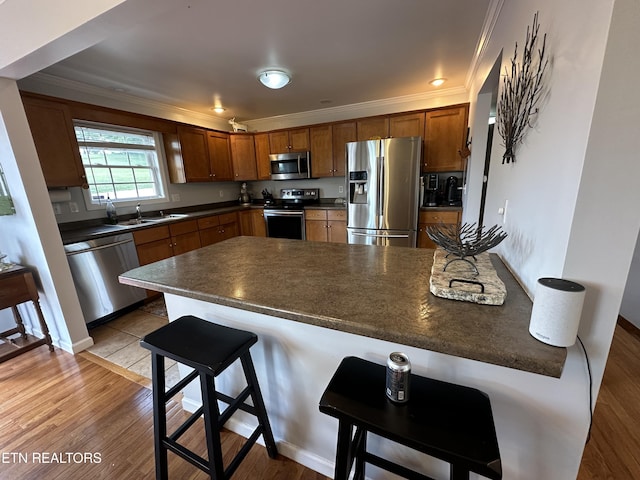kitchen featuring a breakfast bar, ornamental molding, a peninsula, dark countertops, and appliances with stainless steel finishes