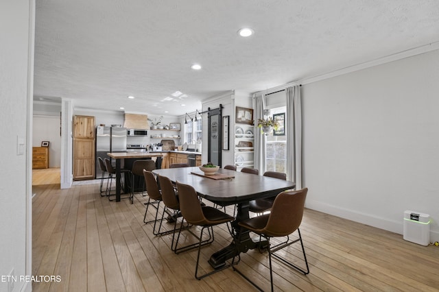 dining space featuring a textured ceiling, light wood-style flooring, baseboards, and ornamental molding