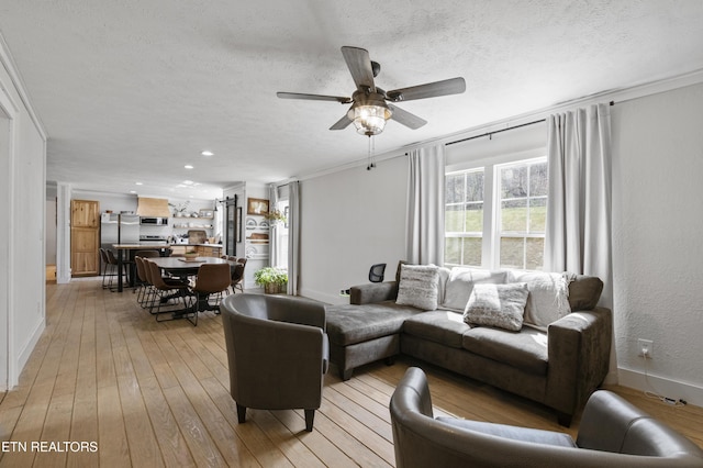 living area featuring crown molding, light wood-style flooring, a ceiling fan, and a textured ceiling