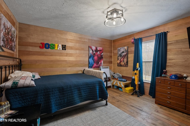 bedroom featuring wood walls, a textured ceiling, and wood-type flooring