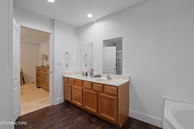 full bathroom featuring double vanity, wood finished floors, crown molding, and a sink