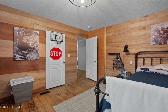 bedroom with visible vents, wood walls, a textured ceiling, and hardwood / wood-style floors