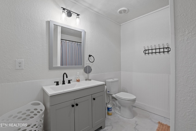 full bathroom featuring a wainscoted wall, toilet, vanity, and a textured wall