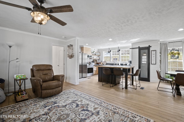 living area featuring a barn door, ornamental molding, a ceiling fan, and light wood finished floors