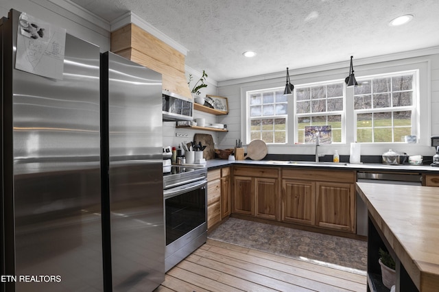 kitchen featuring ornamental molding, a sink, stainless steel appliances, light wood-style floors, and butcher block counters