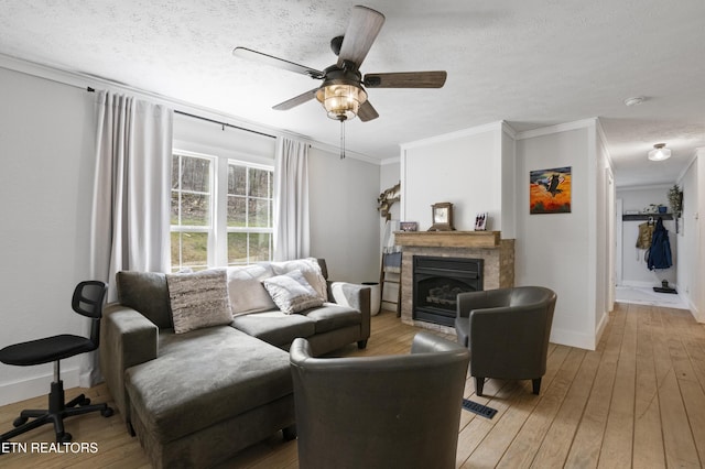 living area featuring crown molding, light wood-style flooring, a brick fireplace, and ceiling fan